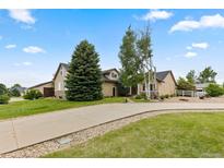 Inviting home featuring a well-manicured lawn, mature trees, and a spacious driveway leading to the attached garage at 8007 Sunrise Cir, Frederick, CO 80516