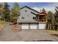 View of a gray two-story home with three garage doors and a wooden porch at 8626 Junco Trl, Evergreen, CO 80439