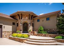 Stunning stone front entrance featuring a decorative door, stone archway, and meticulously landscaped surroundings at 6194 Falcon Ridge Way, Morrison, CO 80465