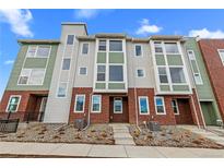 Modern townhome with brick accents and a blend of neutral gray and green siding, set against a bright blue sky at 14281 Currant St, Broomfield, CO 80020
