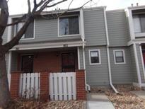 Townhome exterior with gray siding, brick accents, white picket fence and landscaped with rocks and greenery at 7474 E Arkansas Ave # 18-12, Denver, CO 80231