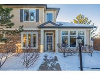 Two-story townhome with stone and siding exterior, snowy landscaping, and a covered entryway at 11261 W Quincy Pl, Littleton, CO 80127