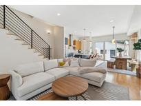 Bright living room featuring an L-shaped couch, modern staircase, and open floor plan flowing into the kitchen and dining area at 2244 S Lincoln St, Denver, CO 80210