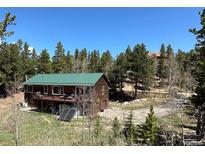 Charming cabin with a green roof, wrap-around balcony and beautiful forest surroundings on a sunny day at 72 Rudi W Ln, Golden, CO 80403