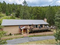 Charming brick home boasts a spacious deck with scenic views of surrounding lush green trees at 7815 Armadillo Trl, Evergreen, CO 80439