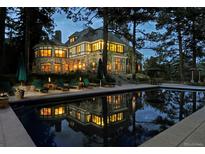 A luxury home featuring an in-ground pool reflecting the house at night, with lounge chairs and trees at 222 Greystone Rd, Evergreen, CO 80439