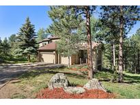 Inviting home with a two-car garage, lush landscaping, and mature trees on a well-maintained property at 2873 Cortina Ln, Evergreen, CO 80439