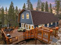 Charming barn style house with a wooden deck featuring outdoor seating, grill, and string lights in a wooded setting at 384 Blue Ridge Rd, Breckenridge, CO 80424