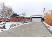 Charming brick home with a wide driveway, attached garage, front porch, and snowy yard at 10799 Murray Dr, Northglenn, CO 80233