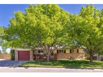 Charming single-story home with brick accents, red garage door, lush lawn, and mature shade trees at 945 W 101St Ave, Northglenn, CO 80260