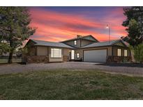 Inviting tan home with stone accents, two-car garage, mature trees, and gravel driveway at dusk at 1866 Mountain View St, Erie, CO 80516
