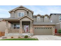 Charming two-story home featuring a covered porch with stone accents and a two-car garage at 16685 E 101St Ave, Commerce City, CO 80022