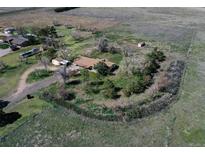 Expansive aerial view of a charming ranch home surrounded by mature trees and lush landscaping in a serene setting at 7409 S County Road 157, Strasburg, CO 80136