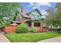 Charming two-story home featuring a brick facade, green trim, a well-manicured lawn, and mature trees at 2201 Cherry St, Denver, CO 80207