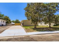Cozy single-story home with a well-manicured lawn, mature trees, and a concrete driveway under a clear blue sky at 311 Harrison Ave, Fort Lupton, CO 80621