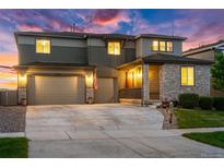 Inviting two-story home with a two car garage, stone accents, manicured lawn, and warm exterior lighting at 12705 Buffington Trl, Parker, CO 80134