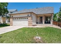 Charming single-story home featuring a well-kept lawn, inviting front porch, and a two-car garage with stylish brick accents at 5033 Goshawk Ct, Brighton, CO 80601