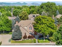 Charming two-story brick home with lush landscaping and mature trees, mountains in the background at 7425 S Utica St, Littleton, CO 80128