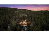 Stunning aerial shot of an illuminated home nestled within a dense forest at dusk at 26806 Evergreen Springs Rd, Evergreen, CO 80439