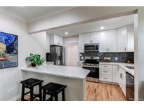 Bright kitchen boasts white cabinets, stainless steel appliances, quartz counters, and eat-in bar at 1969 Uinta St, Denver, CO 80220