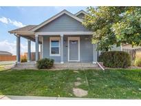 Charming blue home featuring a covered porch, well-maintained lawn, and mature tree at 55490 E 27Th Pl, Strasburg, CO 80136