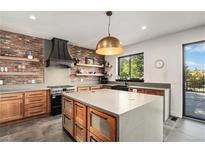Modern kitchen featuring a brick accent wall, stainless steel appliances, floating shelves, and a large center island at 10731 E 151St Pl, Brighton, CO 80602