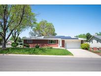 Charming single-story brick home with a well-manicured front lawn, mature trees, and solar panels on the roof at 509 Newland St, Lakewood, CO 80226