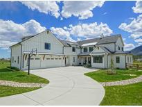 Beautiful white farmhouse exterior with a basketball hoop and long curved driveway at 609 Pioneer Camp Vw, Palmer Lake, CO 80133