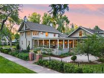 Stunning two-story home with a brick and black metal fence, a beautiful lawn, and a large, inviting wrap-around porch at 3109 E Warren Ave, Denver, CO 80210