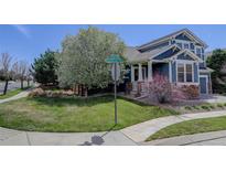 Charming blue home with lush lawn, stone accents, white pillars, and blooming trees create a welcoming curb appeal at 9996 Sedalia St, Commerce City, CO 80022