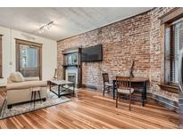 Inviting living room featuring exposed brick wall, fireplace, and hardwood floors at 1210 E Colfax Ave # 206, Denver, CO 80218