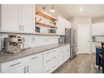 Bright kitchen features white cabinets, floating wood shelves, stainless steel appliances, and stylish countertops at 8395 E 132Nd Pl, Thornton, CO 80602