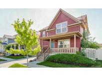 Charming two-story red home featuring a welcoming front porch, well-manicured lawn, and vibrant landscaping at 10712 Dayton Way, Commerce City, CO 80640