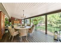Covered deck features wood floors, a dining table, and black metal railing overlooking a lush yard at 730 Crescent Ln, Lakewood, CO 80214