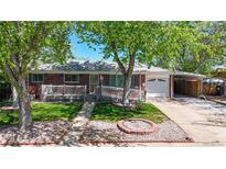 Charming brick home featuring a manicured lawn, mature trees, and a cozy front porch at 14157 E 26Th Ave, Aurora, CO 80011