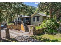 Charming home with a stone wall, wooden deck and stairs, nestled among lush trees at 55 Two Moon Rd, Idaho Springs, CO 80452