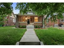 Charming brick home with a well-manicured lawn and inviting walkway under the shade of a large tree at 1245 Garfield St, Denver, CO 80206