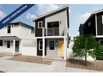 Modern two-story home featuring a balcony, black and gray siding, white trim, and a yellow front door at 13029 E 103Rd Pl, Commerce City, CO 80022