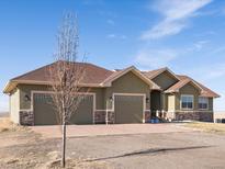Beautiful single-story home with three-car garage, stone accents and a spacious driveway on a sunny day at 14077 Indianfield Ct, Hudson, CO 80642