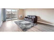 Bright living room with a sliding glass door to balcony, wood floors and dark sofa on a patterned rug at 2231 S Vaughn Way # 114B, Aurora, CO 80014