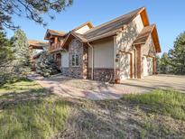 Stunning home featuring a stone facade, two-car garage, and an inviting walkway through a landscaped front yard at 7076 Boreas Rd, Larkspur, CO 80118
