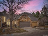 Charming home featuring a stone accent wall above the garage door and a beautiful sunset in the background at 10000 E Yale Ave # 58, Denver, CO 80231