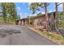 Brick home with an asphalt driveway is surrounded by mature trees and well-maintained landscaping at 7845 Armadillo Trl, Evergreen, CO 80439