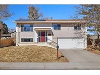 Split-level home featuring neutral siding, a red front door, attached garage, and a well-maintained front yard at 12843 W Jewell Cir, Lakewood, CO 80228