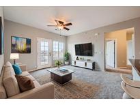 Bright living room featuring a ceiling fan, a flat-screen TV, balcony access, and neutral-toned decor at 2705 S Danube Way # 306, Aurora, CO 80013