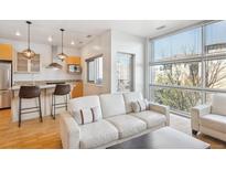 Bright open-concept living room featuring a modern kitchen, breakfast bar, and oversized windows with natural light at 2958 Syracuse St # 316, Denver, CO 80238