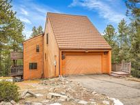Exterior view showcasing the home's garage and wooden siding, surrounded by a wooded landscape at 23485 Bluestem Dr, Golden, CO 80401