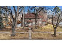 Brick home with tile roof, mature trees, and a black metal fence at 1650 Monaco St Pkwy, Denver, CO 80220