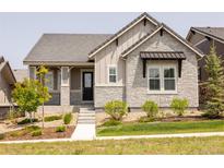 Charming home featuring stone accents, covered porch, tidy landscaping, and a well-maintained front lawn at 997 Brocade Dr, Highlands Ranch, CO 80126