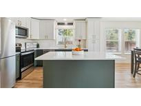 Modern kitchen features white cabinets, a center island, stainless steel appliances, and light hardwood flooring at 3866 S King St, Denver, CO 80236